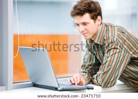 Casual looking businessman working on laptop computer in front of office window.