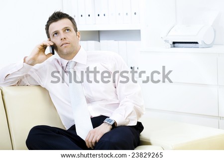 Mature businessman sitting on sofa and calling on mobile phone at office.