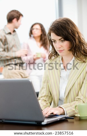 Team of young successful business people talking and drinking coffee at office, businesswoman working on laptop computer in front.