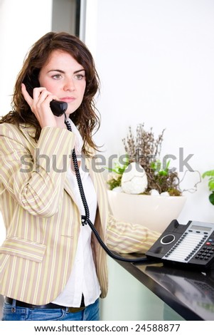 Young female receptionist receiving phone calls at office reception.