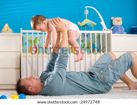 Father lying on back and lifting baby boy ( 1 year old ) at home in children\'s room.