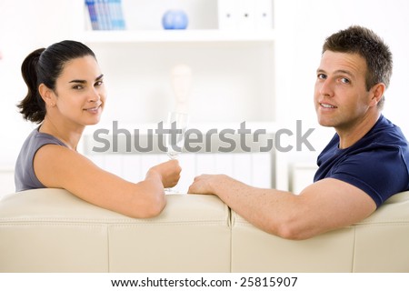 Love couple drinking champagne at home on sofa. Smiling and looking at camera.