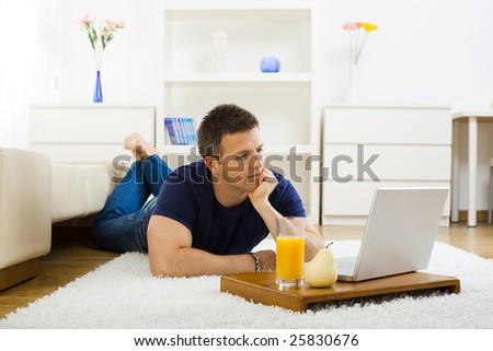 Casual young man working at home on his laptop computer, lying on floor and leaning on hand.