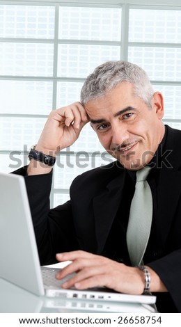 Gray haired creative director working on laptop computer at office, smiling.