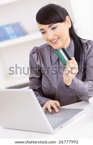 Smiling young women shopping online at home, using laptop computer, holding credit card in hand.