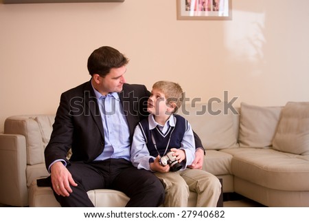 Father and son wearing a digital camera sitting together on couch at home, looking at each other.