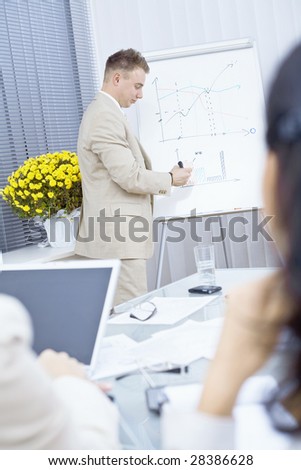 Young businessman doing business presentation, drawing and explaining charts on whiteboard in meeting room.