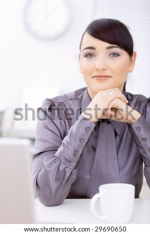 Young businessman sitting at desk at office, thinking, smiling.