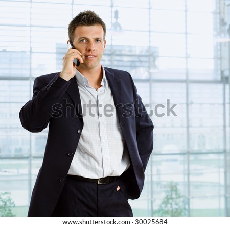 Businessman talking on mobile phone in front of office window.
