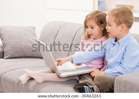Amazed siblings sitting on couch at home, browsing internet on laptop computer. Boy pointing to screen.