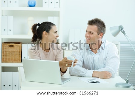 Young casual couple sitting  at desk working together at home office, smiling, happy, using laptop computer.