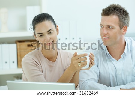 Young casual couple sitting  at desk working together at home office, smiling, happy, using laptop computer.