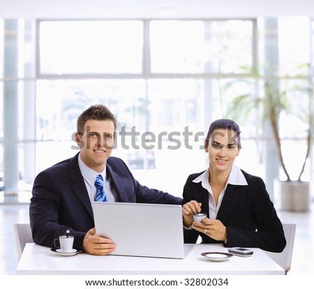 Businessman and businesswoman having a meeting in office lobby, drinking coffee.