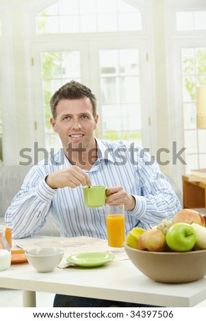 Young man having healthy breakfast, drinking coffee, orange juice and reading newspaper.