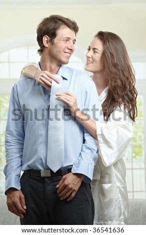 Young woman helping to fasten her boyfriend\'s tie, looking at each other smiling.