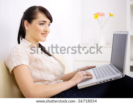 Young women sitting on couch at home and browsing internet on laptop computer, smiling.