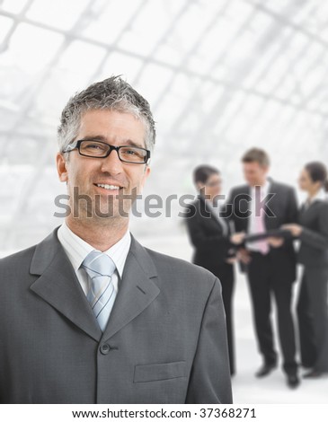 Portrait of happy businessman standing  in office hallway, smiling.