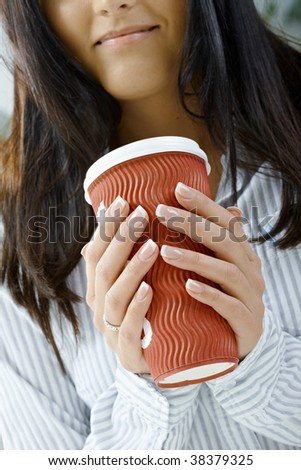 Closeup portrait of young woman holding a red mug. Selective focus on hands and fingers.