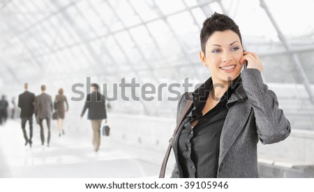 Happy businesswoman talking on mobile phone on office hallway, smiling.