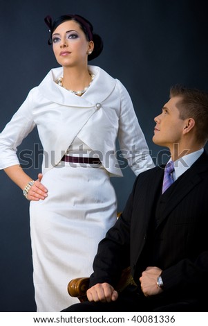 Portrait of young couple dressed in elegant clothes. Woman wearing white cocktail shirt with jacket, man wearing three-pieces dark suit.