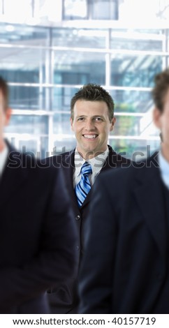 Happy businessman standing behind other businesspeople, in front of office building.