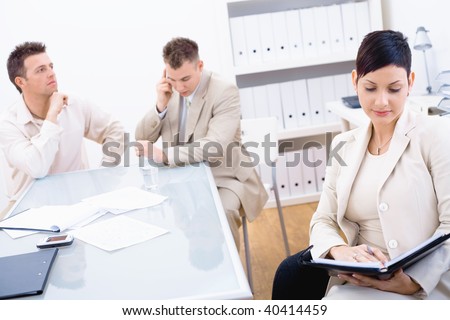 Young businesspeople sitting at office desk. Businesswoman looking at personal organizer, businessman talking on mobile.