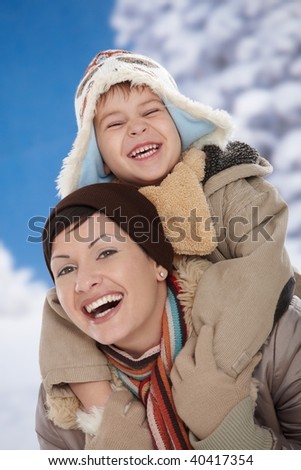 Portrait of happy mother and child  together in snow on a cold winter day laughing, smiling.