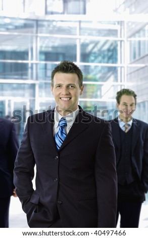 Happy businessman standing in front of office building, smiling.