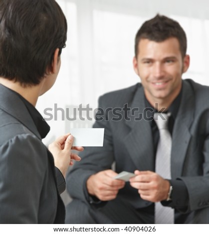 Business meeting at office lobby, people sitting on sofa changing business cards. Focus on card.