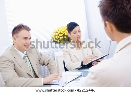 Happy businesspeople conducting job interview in brightly lit office, smiling.