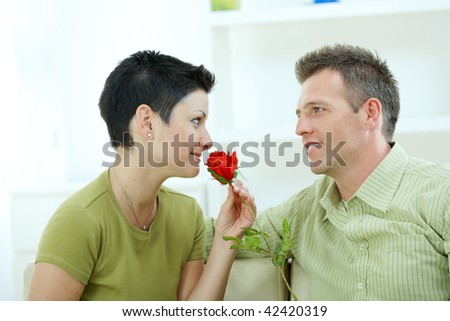Romantic man giving red rose to woman at home, smiling.