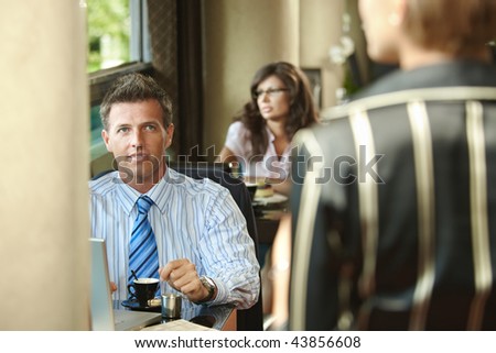 Young businessman waiting at cafe table drinking coffee,  businesswoman arriving for the meeting.
