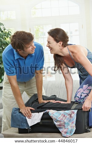 Happy Couple packing for holiday, trying to close suitcase full with clothes.