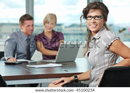 Smiling businesswoman on business meeting at office with team in background.