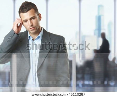 Troubled businessman standing in office lobby, thinking.