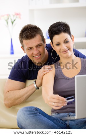 Couple using laptop computer at home together, looking at screen, smiling.