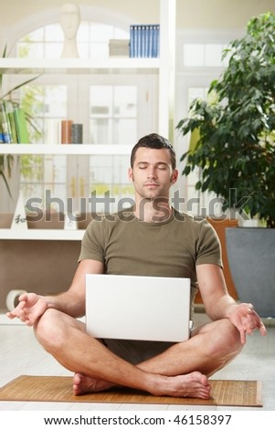 Man sitting in yoga position and meditating,holding laptop computer on his knee.