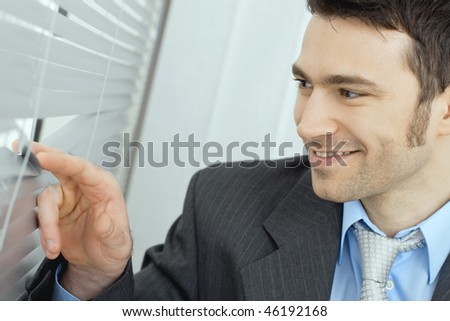 Closeup of happy businessman looking out the window through rolling shutter, smiling.