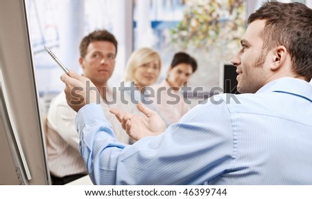 Young businessman speaking on business presentation in meeting room, pointing with pen, explaining, side view.