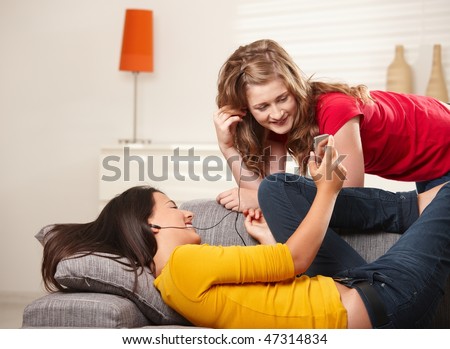Smiling teen girls with earphones looking at phone on the couch at home.