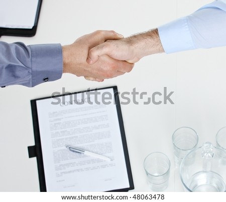 Closeup of hands, businessmen shaking hand over contract on meeting table in office.