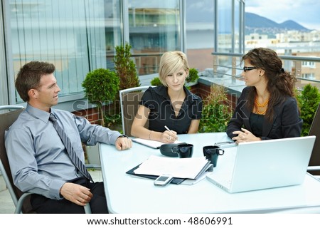 Group of young business people sitting around table on office terrace outdoor, talking and working together.