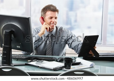 Happy businessman having conversation on landline phone looking at family photo smiling.