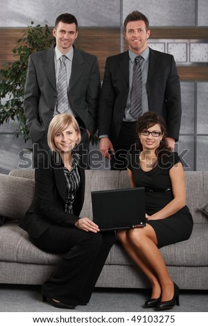 Portrait of happy business team in office, people sitting on sofa smiling, looking at camera.