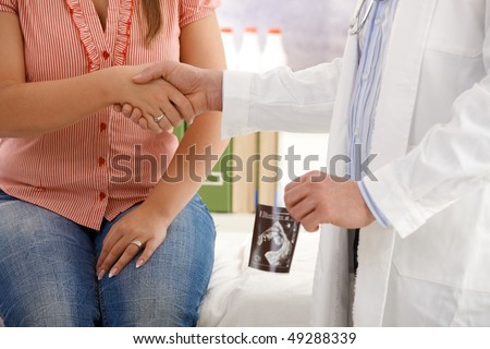 Pregnant woman shaking hands with doctor after consultation, doctor holding ultrasound photo of baby.
