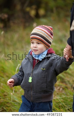 Kid in coat and cap walking hand in hand outdoor in autumn forest.