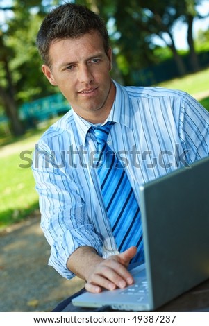 Casual businessman using laptop computer in park summertime.