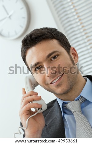 Happy young businessman talking on landline phone at office, smiling.