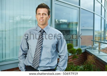 Businessman standing on office terrace outdoor, looking at camera, smiling.