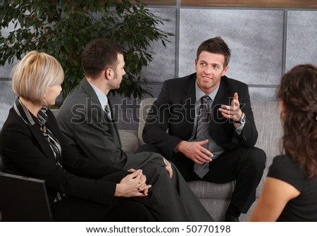 Smiling businesspeople having meeting sitting on sofa in office, listening to executive talking.